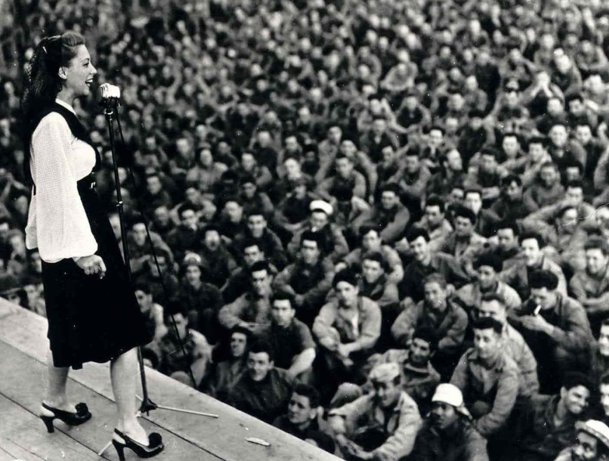 A female USO performer sings to a crowd of soldiers