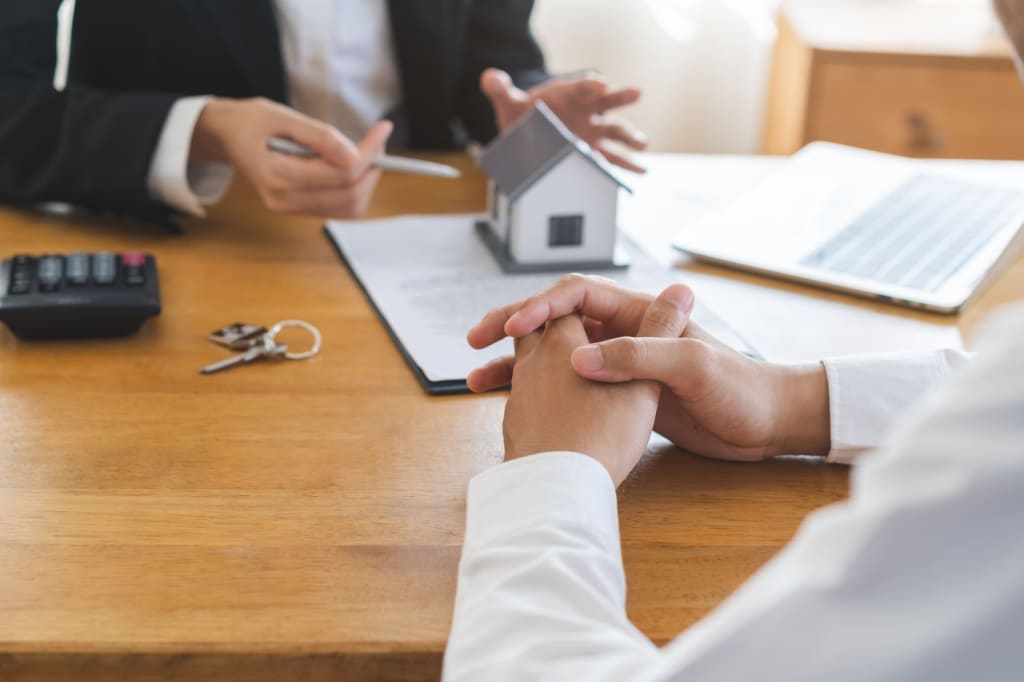 due persone parlano di case su un tavolo con fogli e modellino di casa