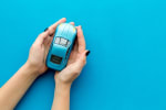 mani_con_auto_azzurra_in_miniatura_su_sfondo_azzurro