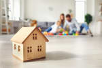 casa-in-miniatura-in-legno-con-famiglia-sullo-sfondo