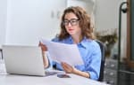 Donna con occhiali che legge documenti davanti al computer