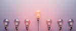 Fila di lampadine con lampadina centrale accesa su sfondo rosa Fila di lampadine con lampadina centrale accesa su sfondo rosa