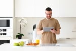 giovane uomo in piedi in cucina utilizza tablet
