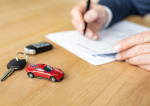 mano che firma un foglio con vicino un auto giocattolo