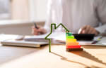modellino casa con scala di classi energetiche e persona che effettu calcoli sullo sfondo
