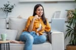 Ragazza sorridente che naviga in internet da pc seduta sul divano di casa