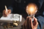 Uomo che tiene in mano una lampadina e fa conti sulle spese luce e gas 