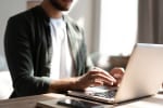 Uomo digita su tastiera laptop