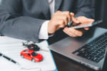 uomo digita sullo smartphone con modellini di auto e pc sullo sfondo