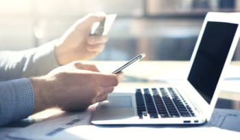 persona con carta di credito in mano utilizza pc e smartphone persona con carta di credito in mano utilizza pc e smartphone