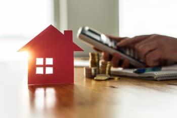 Modellino casa con monete a fianco e persona che calcola il prezzo