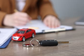 persona firma assicurazione auto con modellino e chiavi