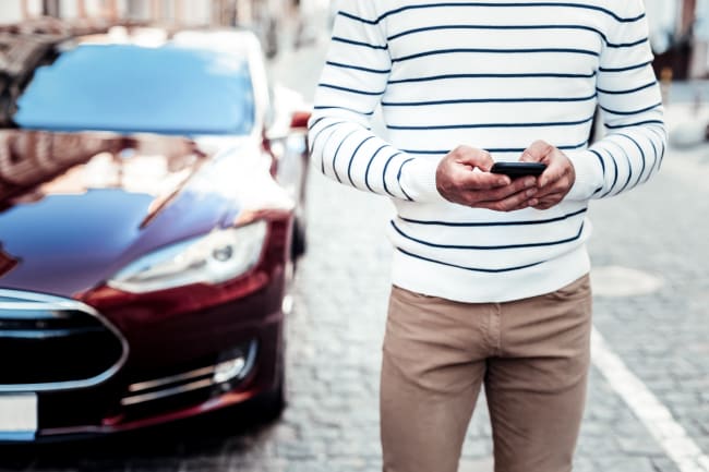 Persona accanto a un'auto che utilizza lo smartphone Persona accanto a un'auto che utilizza lo smartphone