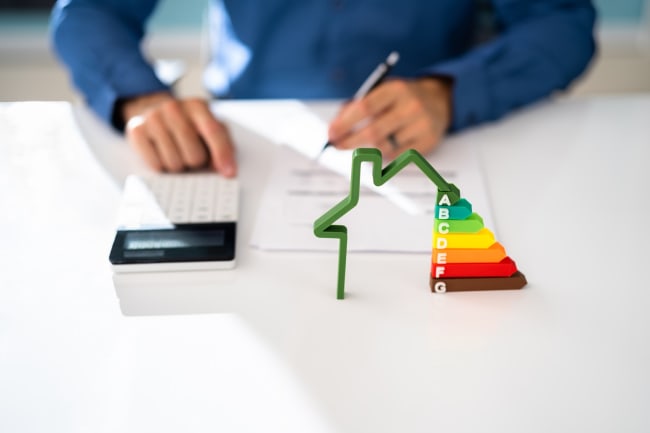 Casa in miniatura con scala classi energetiche e persona che effettua calcoli Casa in miniatura con scala classi energetiche e persona che effettua calcoli