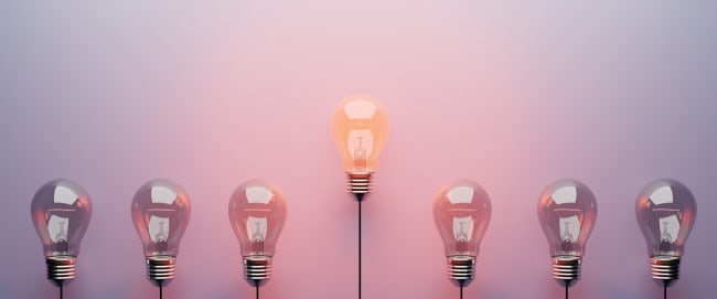 Fila di lampadine con lampadina centrale accesa su sfondo rosa Fila di lampadine con lampadina centrale accesa su sfondo rosa