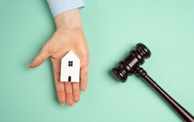 mano tiene modellino di casa con accanto martelletto del giudice mano tiene modellino di casa con accanto martelletto del giudice