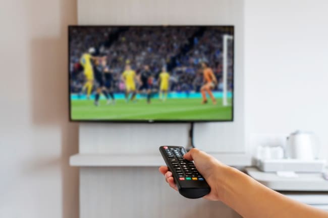 Persona che guarda una partita di calcio in tv e tiene il telecomando in mano Persona che guarda una partita di calcio in tv e tiene il telecomando in mano