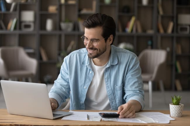 Ragazzo che sorride al pc mentre guarda i suoi guadagni Ragazzo che sorride al pc mentre guarda i suoi guadagni