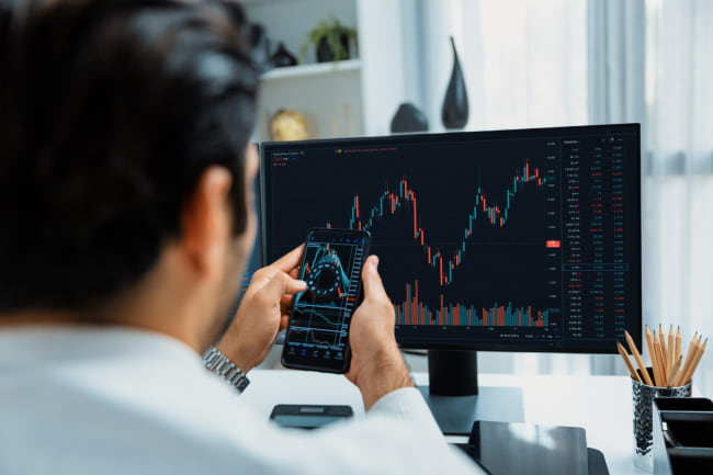 uomo controlla grafici finanziari da pc e cellulare uomo controlla grafici finanziari da pc e cellulare