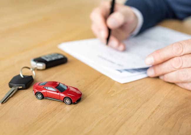 mano che firma un foglio con vicino un auto giocattolo mano che firma un foglio con vicino un auto giocattolo