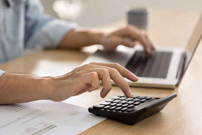 uomo digita su calcolatrice e pc uomo digita su calcolatrice e pc