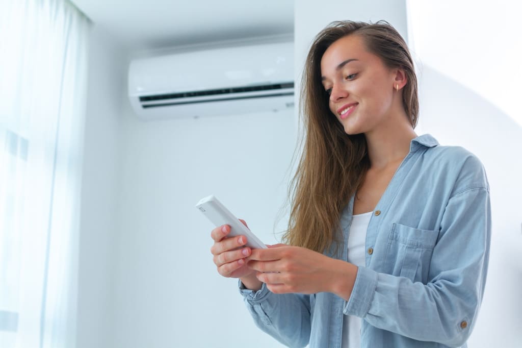 Ragazza che regola il condizionatore con il telecomando Ragazza che regola il condizionatore con il telecomando