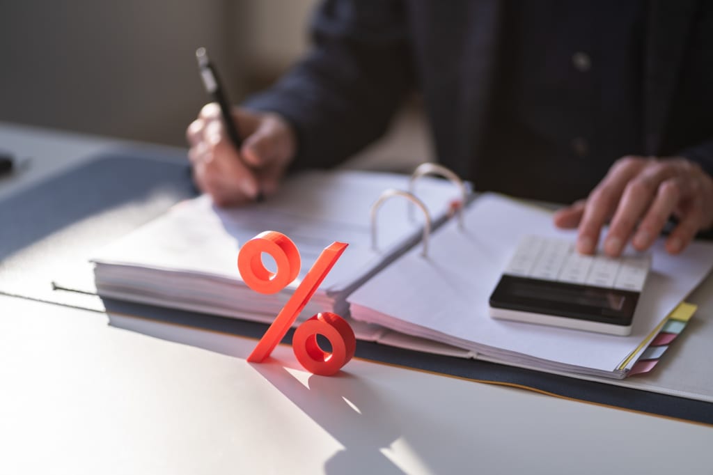 Persona che effettua calcoli sui tassi di interesse con simbolo della percentuale in primo piano Persona che effettua calcoli sui tassi di interesse con simbolo della percentuale in primo piano