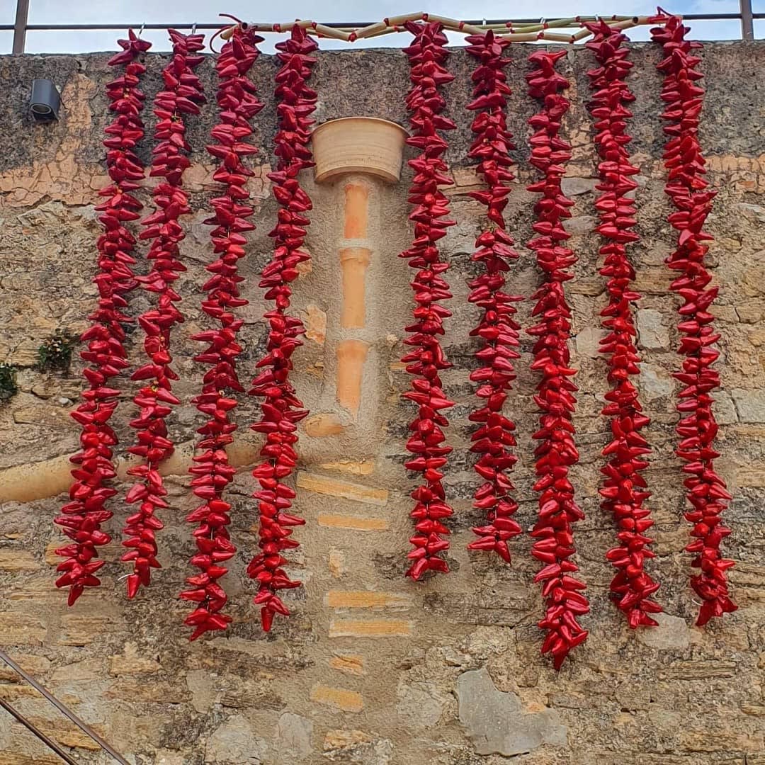 Strings of Tap de Cortí peppers hanging to dry on a stone house facade in Sant Jordi, Mallorca