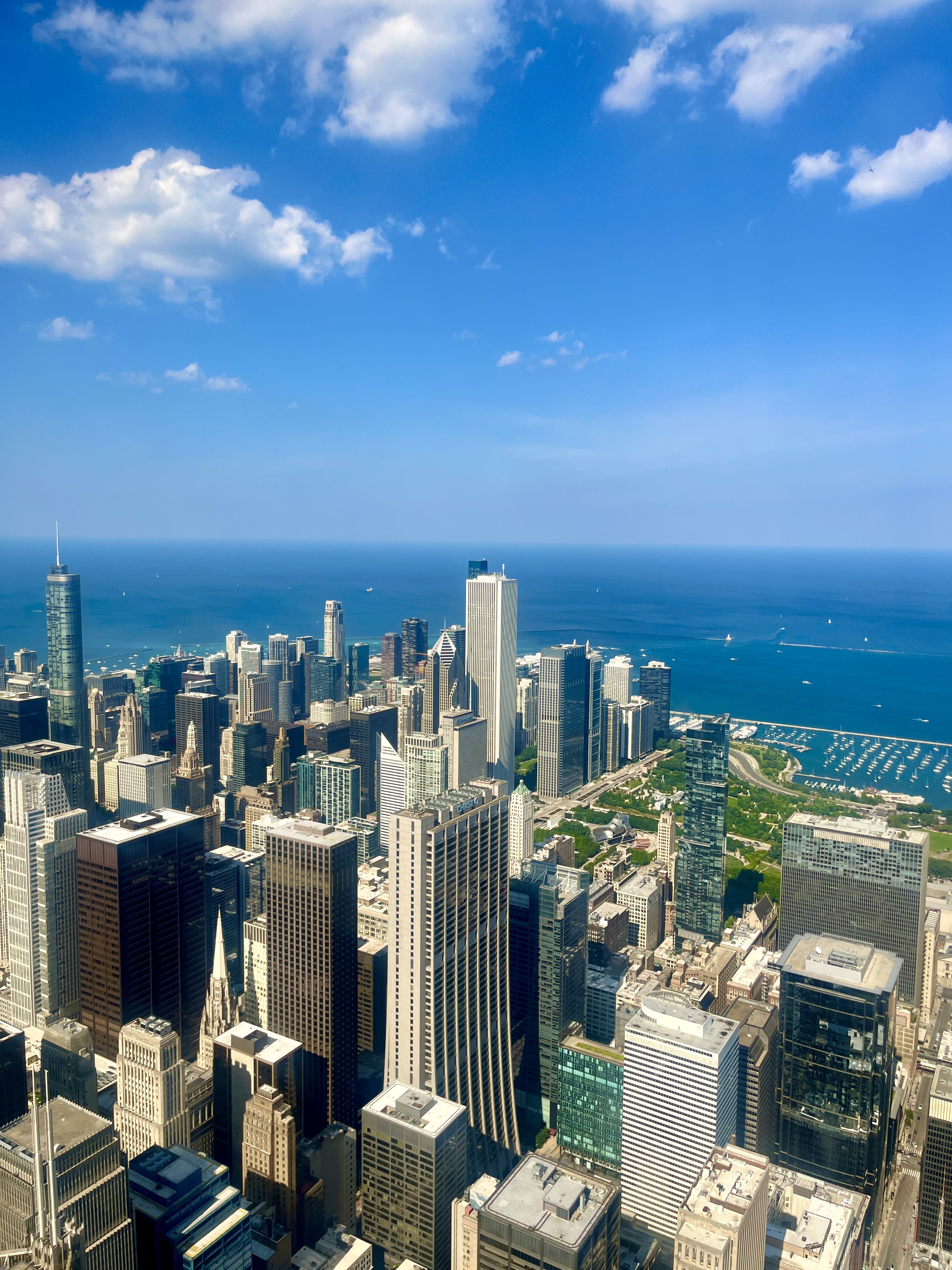 Aerial view of Chicago’s downtown Loop district on a sunny day with Lake Michigan visible in the background and white clouds in a bright blue sky