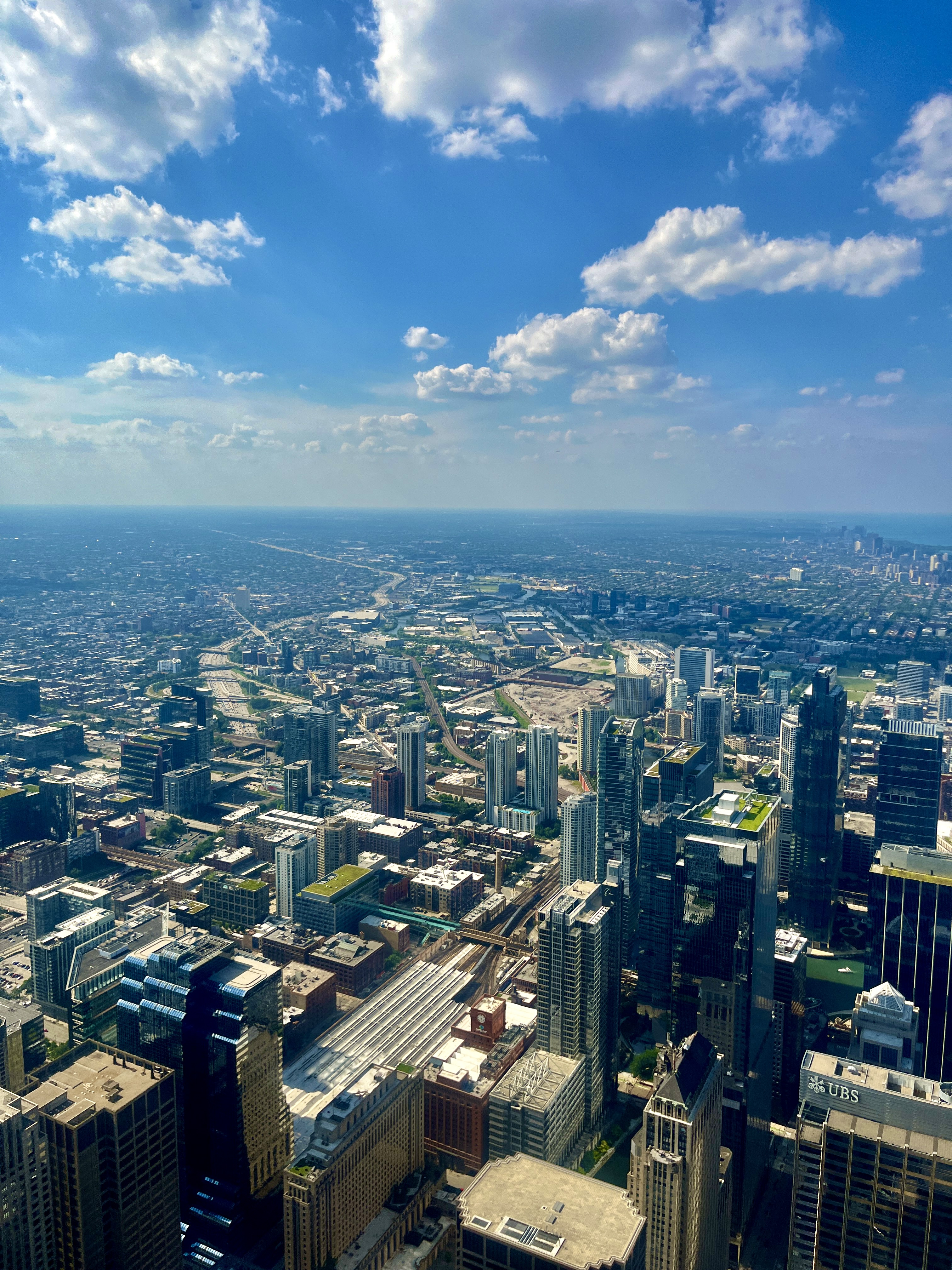 Wide aerial view of Chicago’s urban sprawl stretching to the horizon under a partly cloudy blue sky