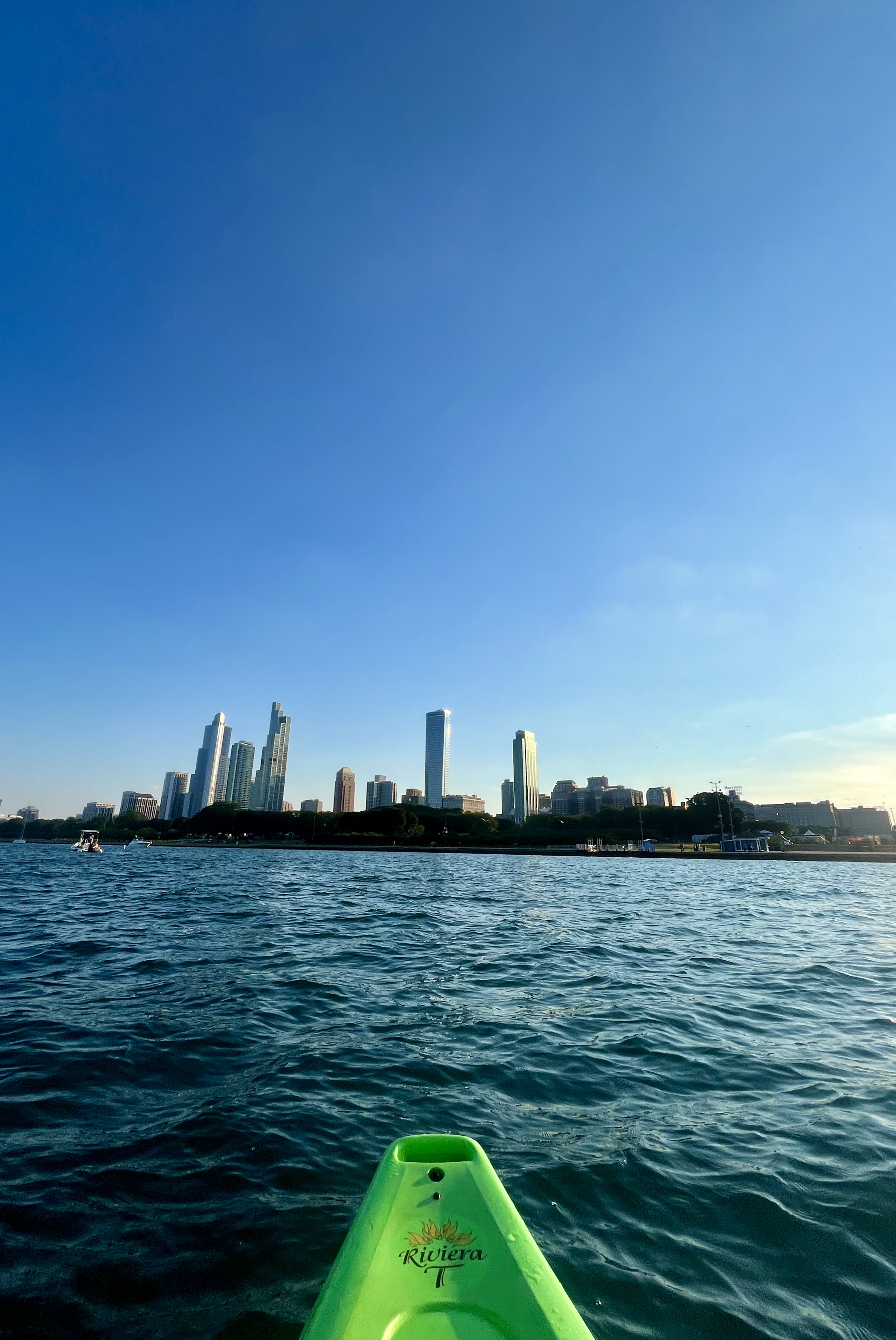 View from a green kayak on a body of water, looking towards a city skyline under a clear blue sky