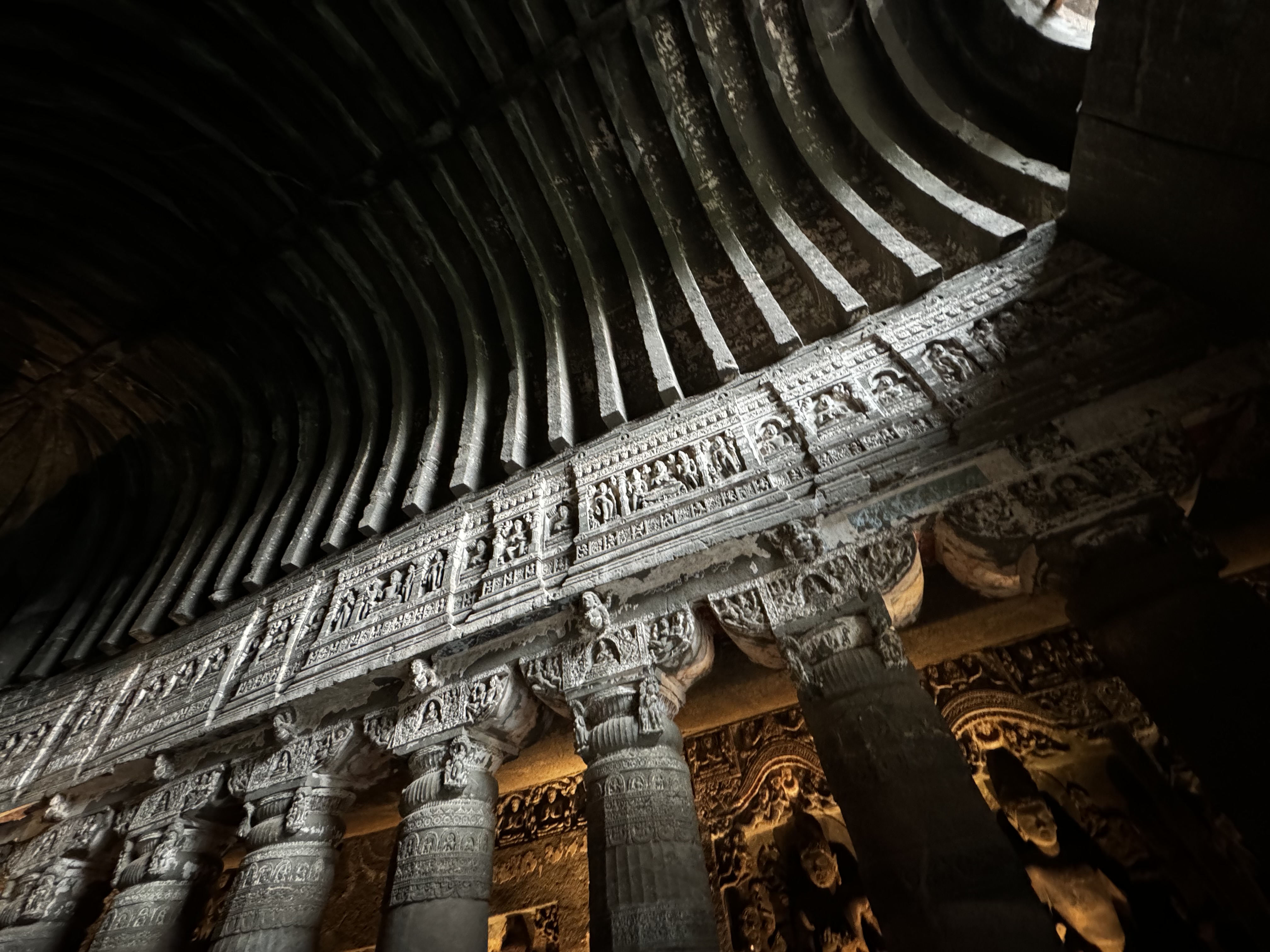 An ultrawide photograph looking up at pillars and the ceiling of the Ajanta caves