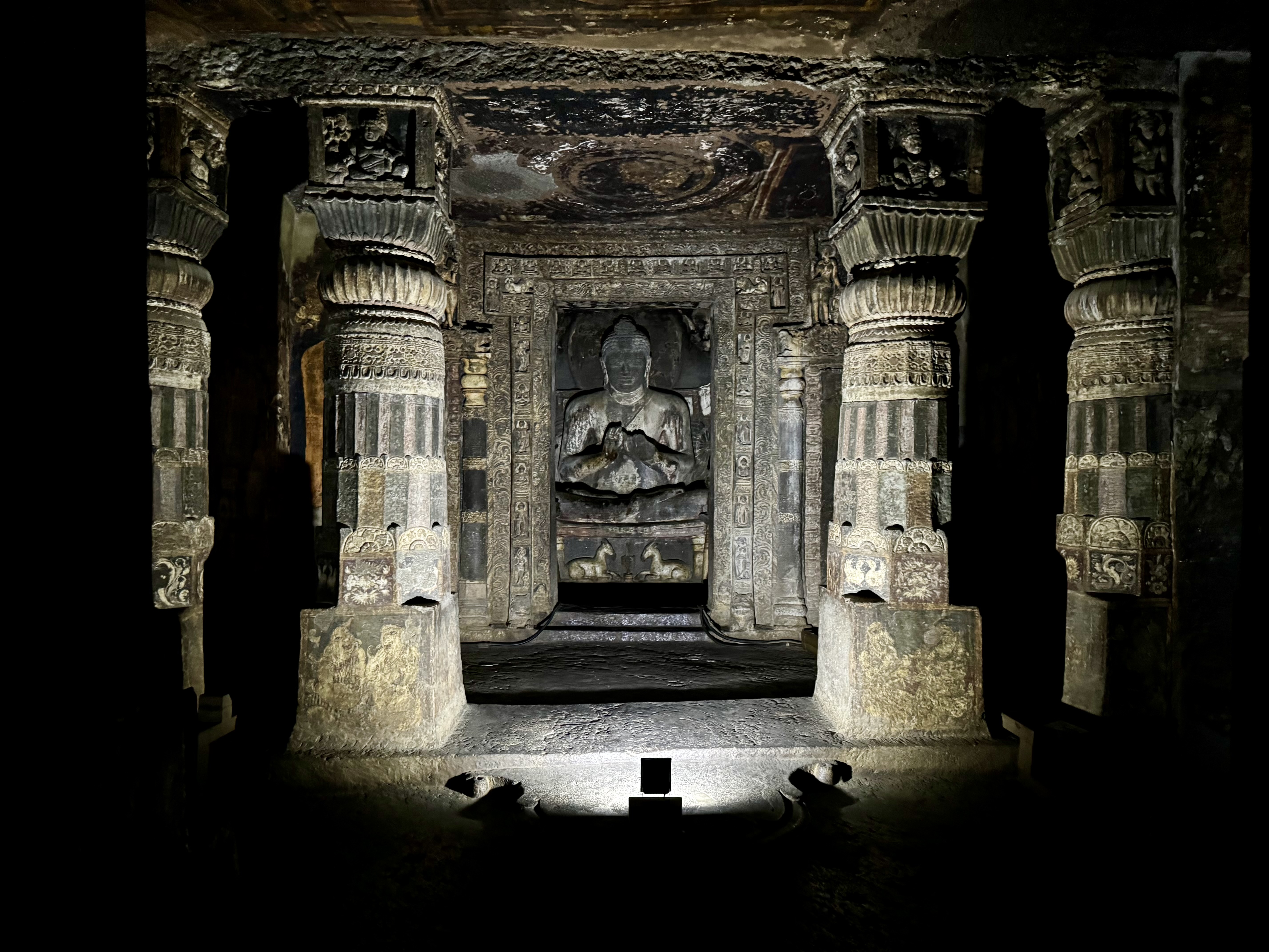 A statue of Buddha illuminated by light centered on it with two pillars on its left and right