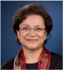 A woman in glasses and a colorful scarf, gazing directly at the camera with a warm expression.