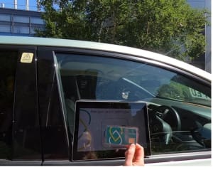 Photo of the outside car window with an embedded touchless device and a user waving a card