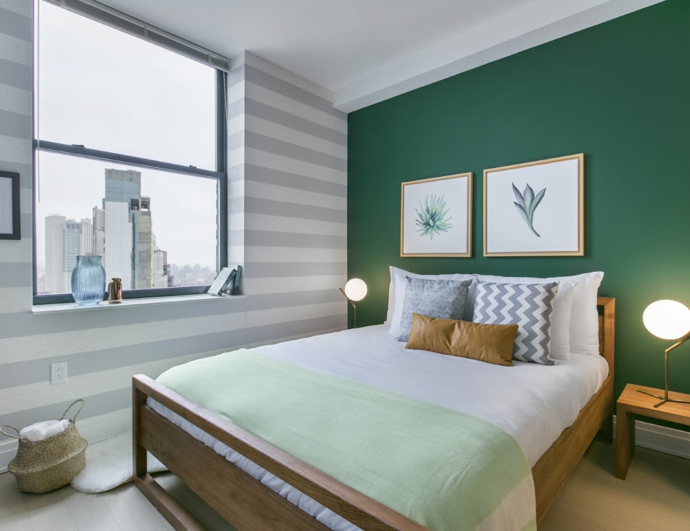 small simple bedroom, dark green accent wall, wooden bedframe, two nightstands with lamps and a city view