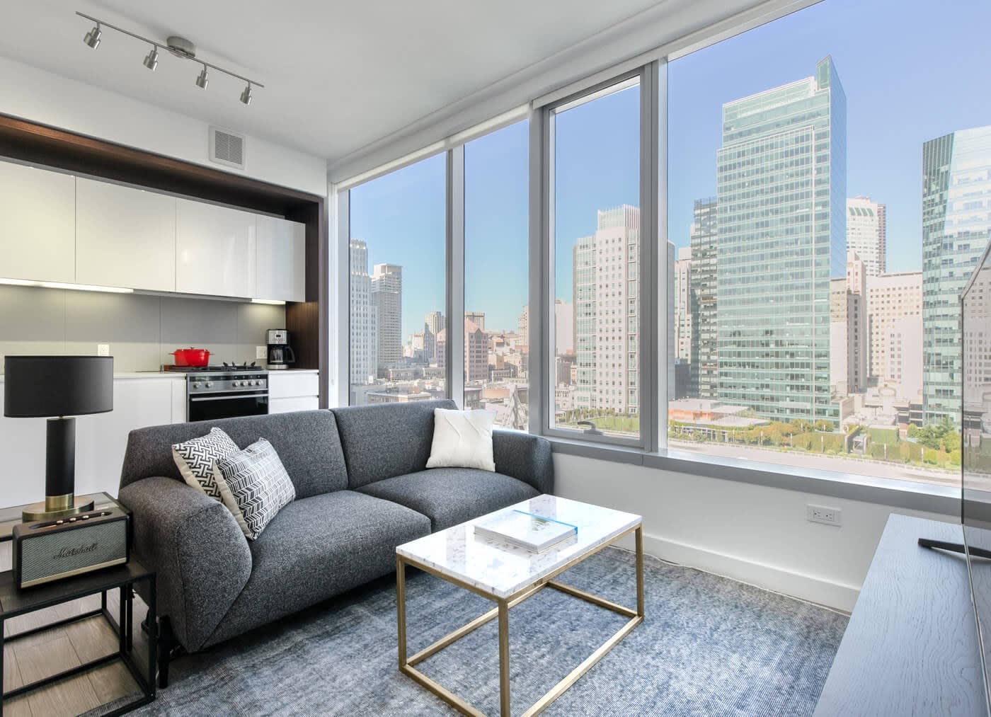 open plan kitchen and living room with a grey couch and a marble coffee table, large window wall with gorgeous city views