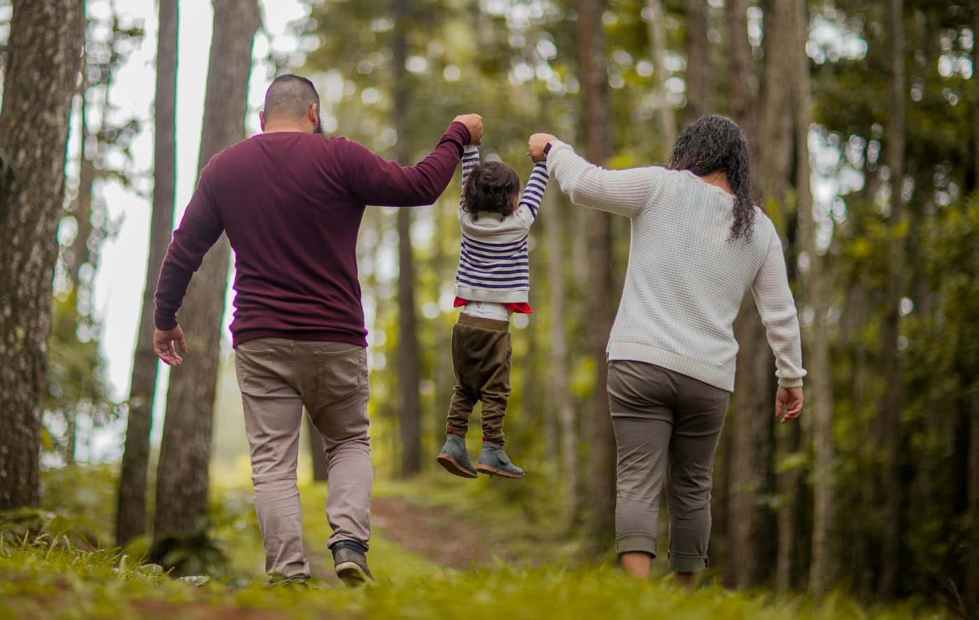 Family swinging kid between them in the woods