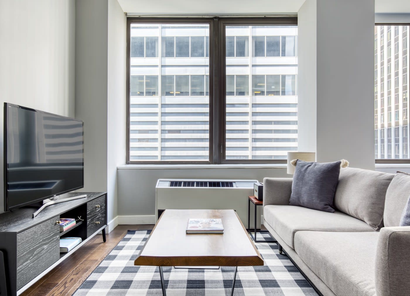 stylish modern apartment, patterned rug with a wooden coffee table on top, grey couch and a black TV unit across from it
