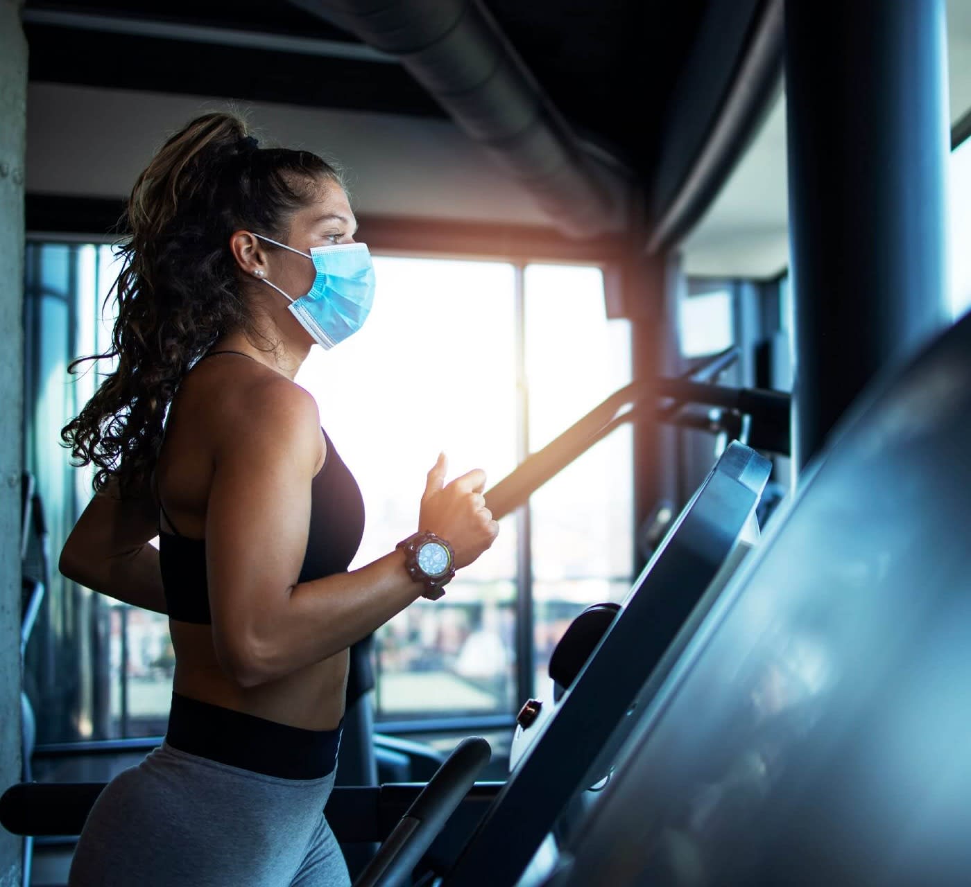 woman in athletic clothes wearing a mask is running on a treadmill at the gym