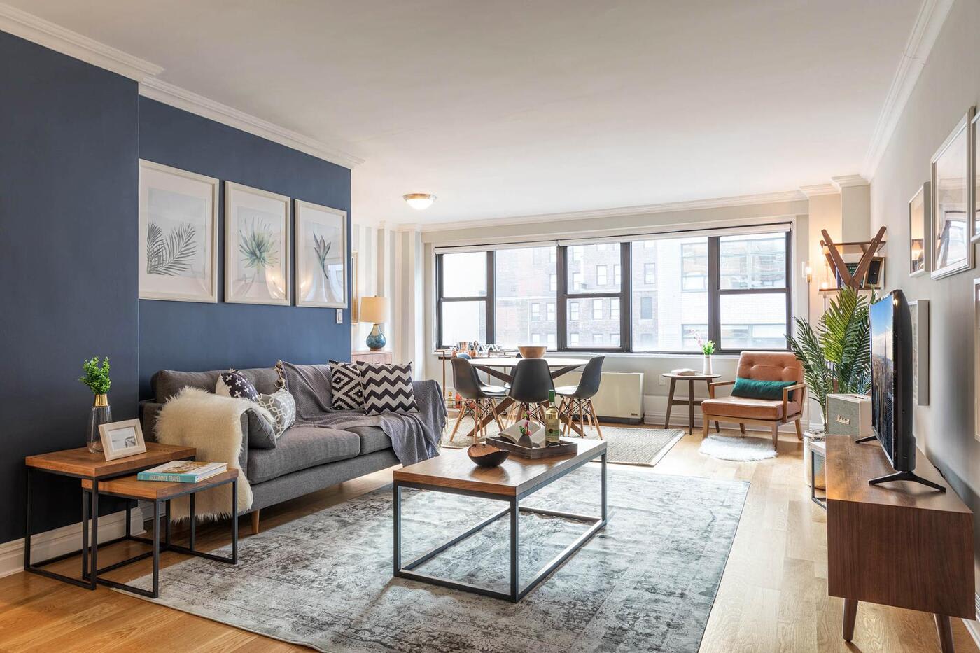 kips bay living room with grey couch striped pillows wooden coffee table a grey rug and a small dining table with 3 black chairs in the back