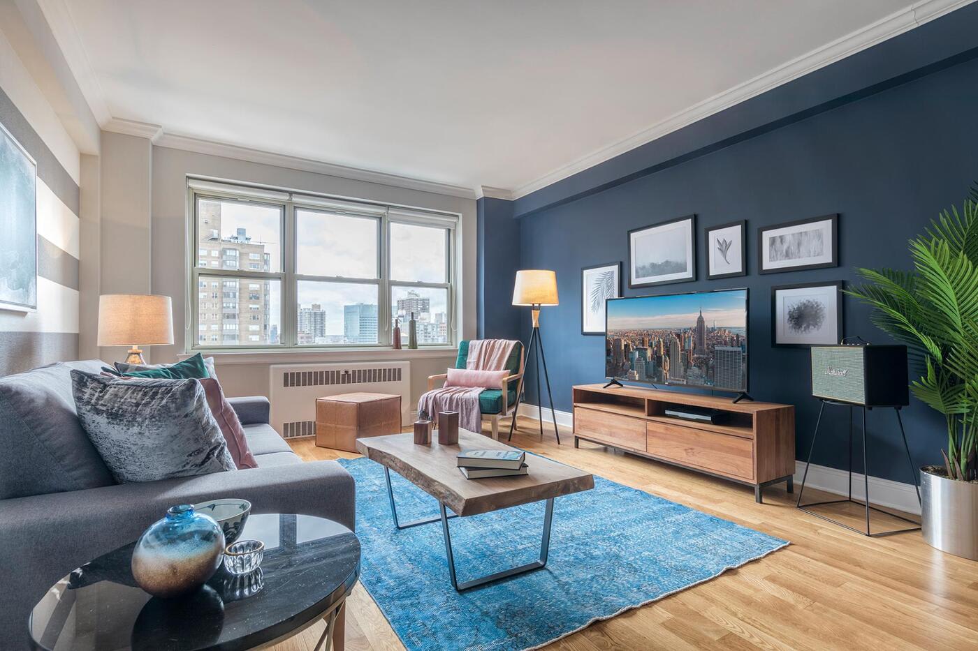 living room with wooden floors grey couch blue rug wooden coffee table and a big TV screen