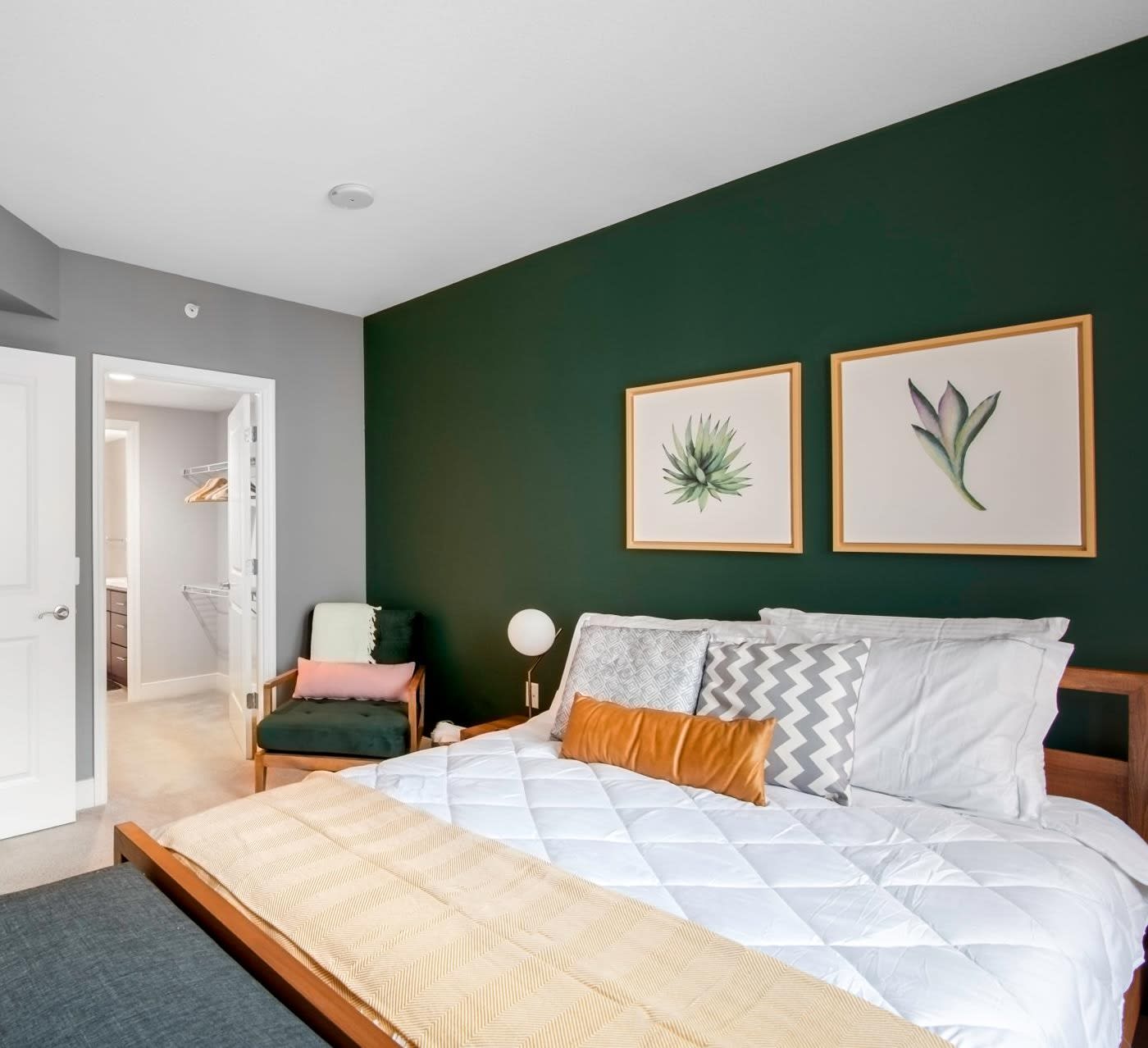 furnished apartment bedroom, dark green accent wall with two paintings, wooden frame bed with white linens and throw pillows