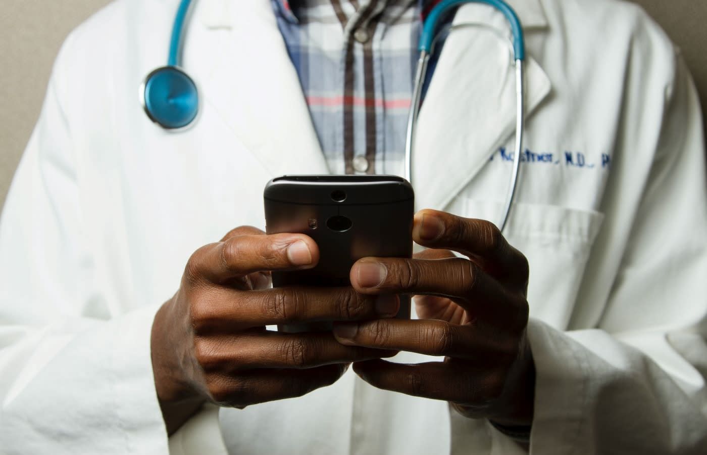 A doctor wearing his white coat texting on a smartphone.