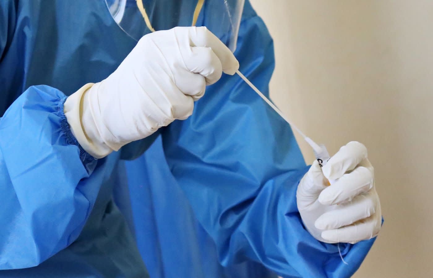 A doctor wearing personal protective equipment testing a nose swab sample.