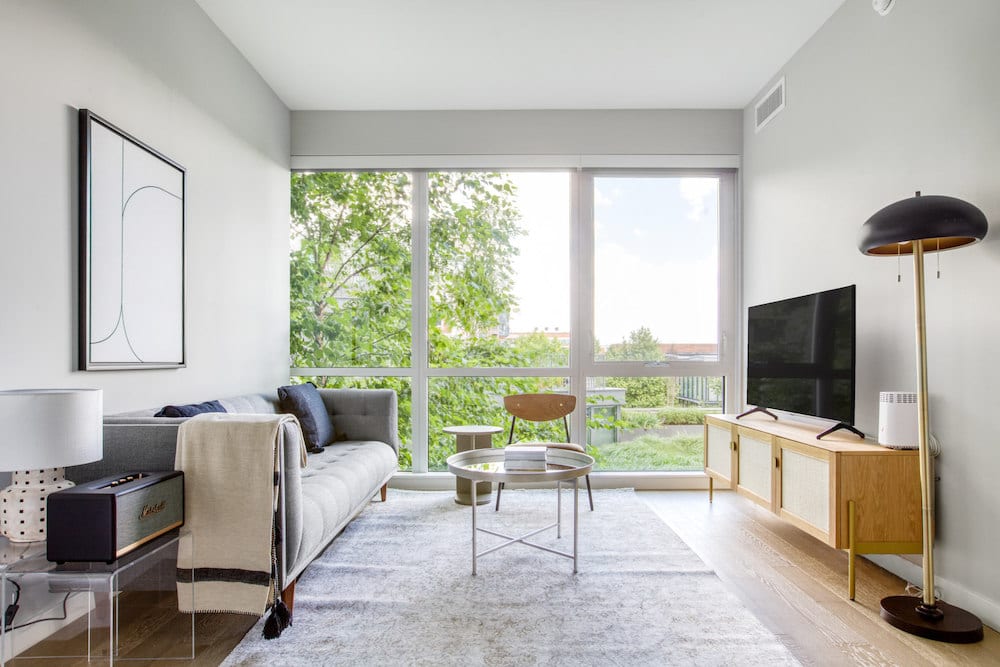 A living room with couch, TV and large windows overlooking a park.
