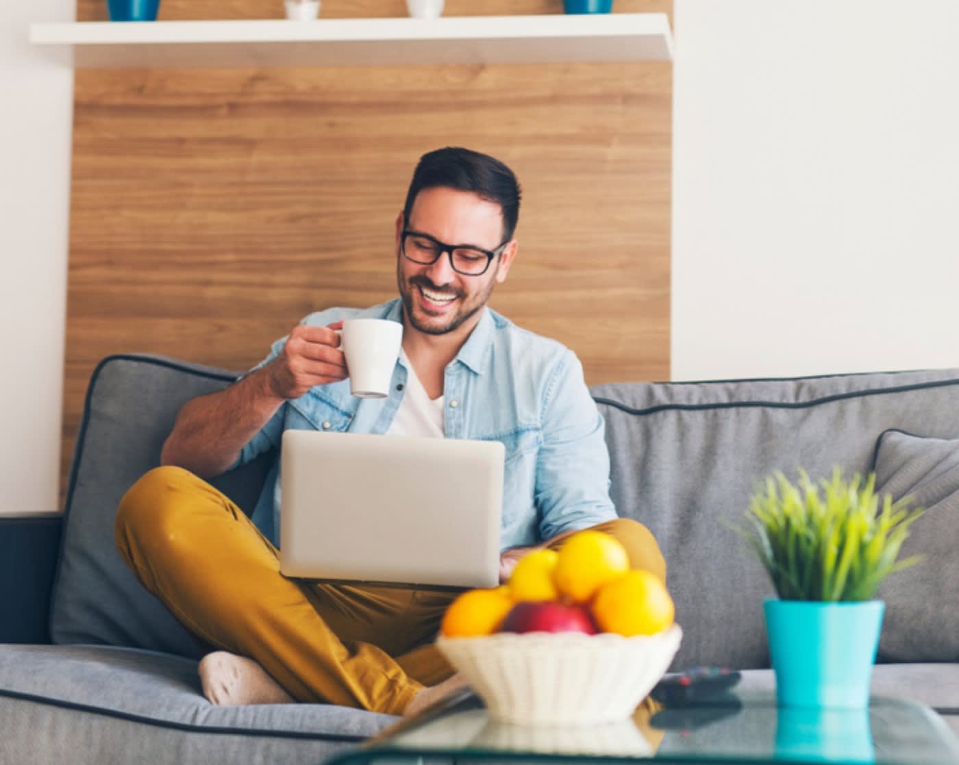 man sitting on couch with laptop and coffee