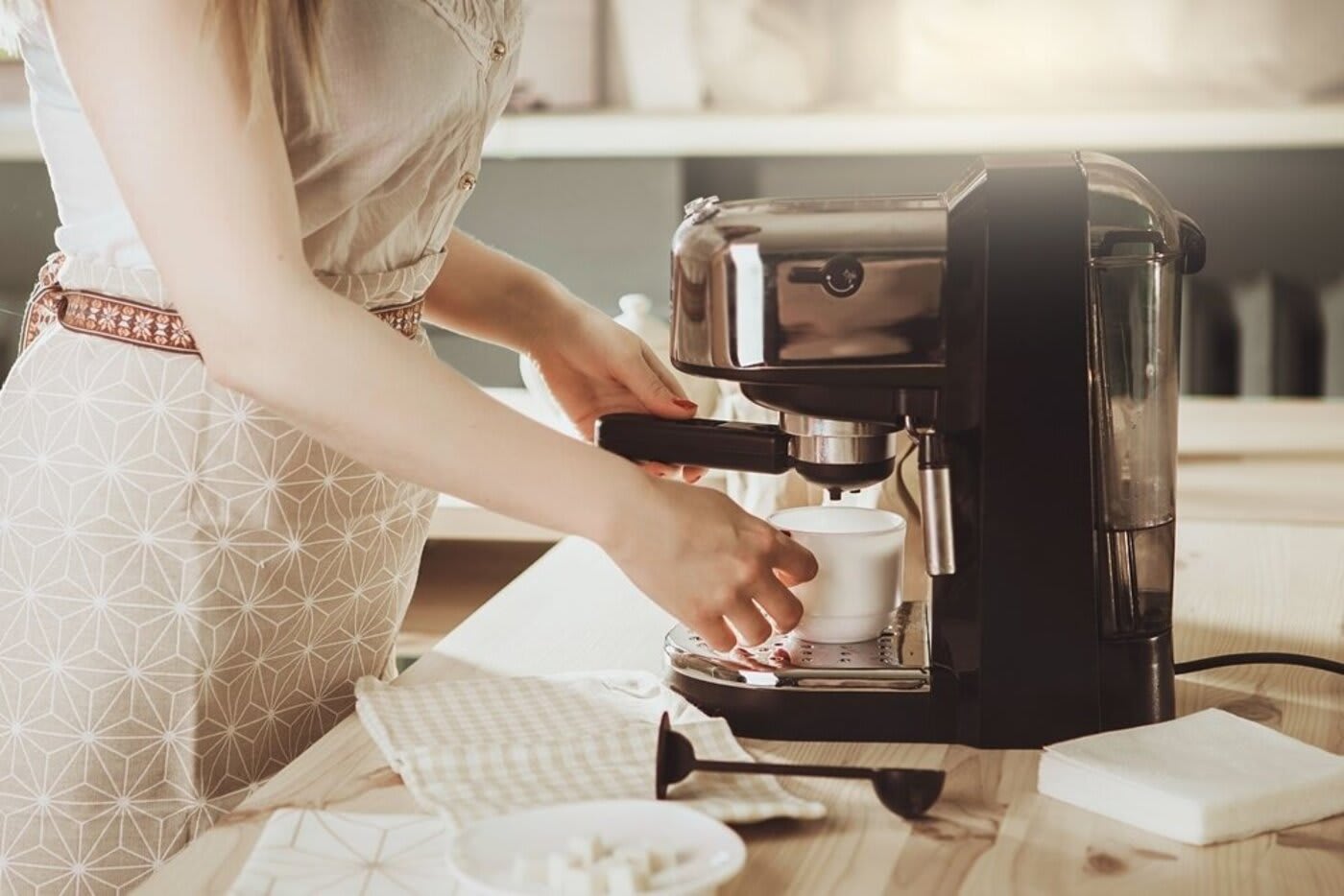 Woman making a cup of coffee in her kitchen with a coffee machine