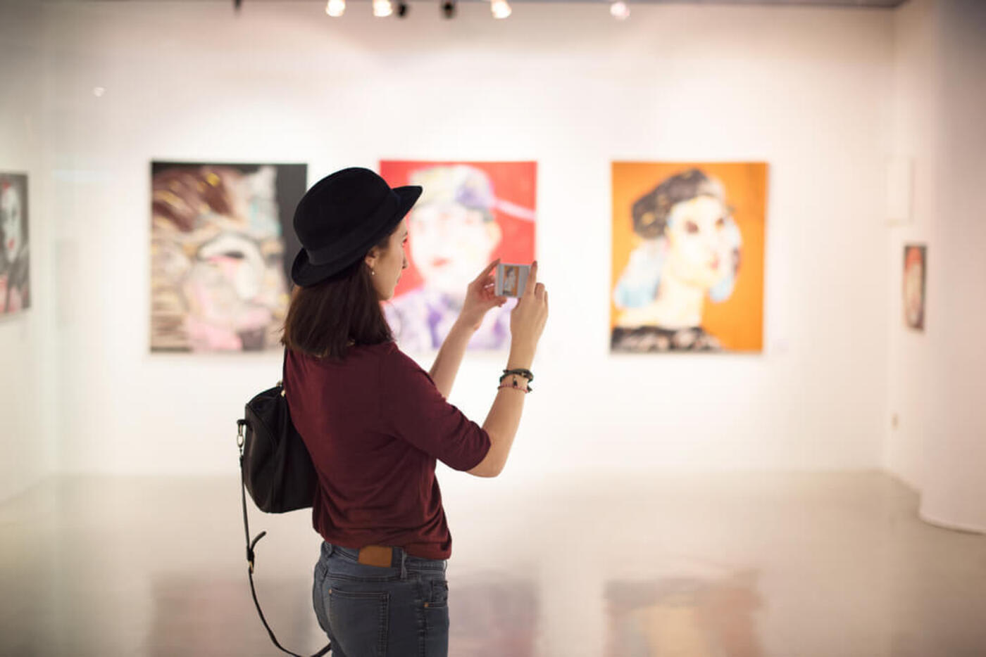 woman stands in art museum looking at the art while holding her smartphone