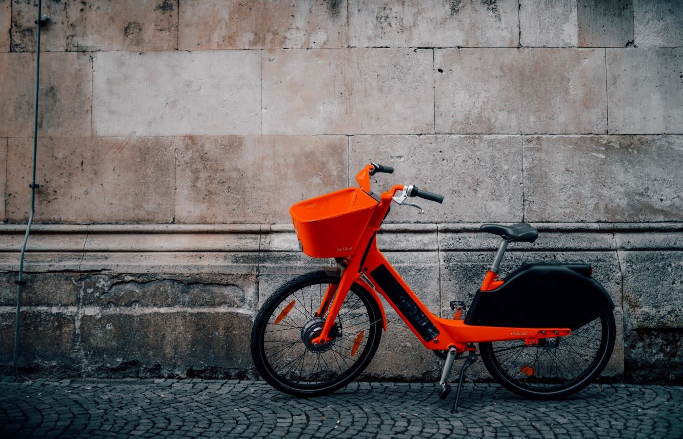 An orange rental bike parked on the side of a cobblestone road.